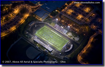 Night time aerial photo of a Friday night high school football game under the lights
